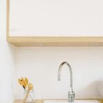 A clean, minimalist kitchen setup featuring a sink with wooden cabinets and modern fixtures.