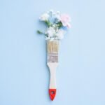 A minimalist image of a paintbrush adorned with delicate flowers against a blue background.