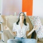 Young woman meditates while sitting among painting supplies, embracing creativity at home.