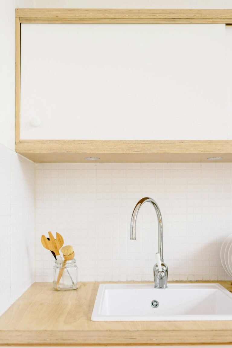 A clean, minimalist kitchen setup featuring a sink with wooden cabinets and modern fixtures.