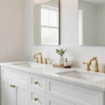 A bright, airy bathroom featuring a white double sink vanity with marble countertop and brass hardware