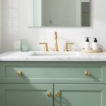A modern bathroom featuring a sage green vanity with brass hardware against white subway tile
