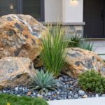 21 Stunning Rock Landscaping Ideas for Front Yard Transformation Modern front yard with large decorative boulders, drought-resistant plants, and river rock mulch creating an elegant rock landscape design