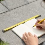 Person measuring and planning a small back patio space with measuring tape and notebook