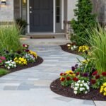 Well-planned front yard landscape with curved borders, flowering plants, and a stone pathway leading to the front door
